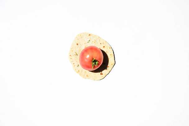 Flat lay of a ripe juicy tomato on a freshly baked homemade chapati, pita bread, flatbread, isolated over white background with copy space for advertising text. Top view, still life, food background - 写真・画像