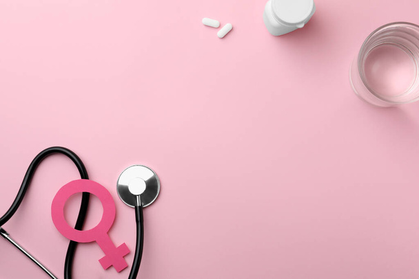 Female gender sign, stethoscope, pills and glass of water on pink background, flat lay. Space for text - Фото, зображення