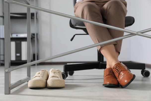 Comfortable sneakers near businesswoman in elegant shoes indoors, closeup - Foto, imagen