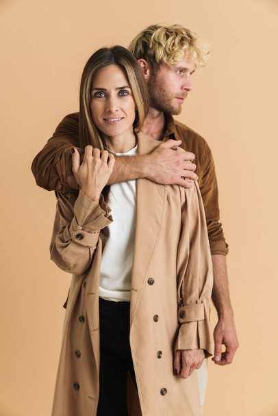 White blonde couple hugging while posing together isolated over beige background - Foto, afbeelding