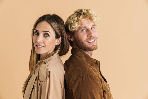White couple smiling at camera while posing back to back isolated over beige background - Fotografie, Obrázek