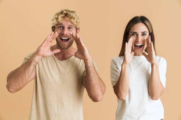 White couple wearing t-shirts gesturing while screaming at camera isolated over beige background - Фото, зображення