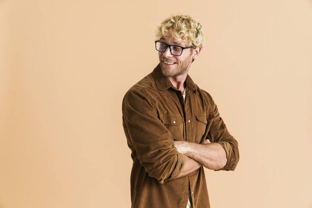 White blonde man in eyeglasses smiling and looking aside isolated over beige background - Foto, Imagem