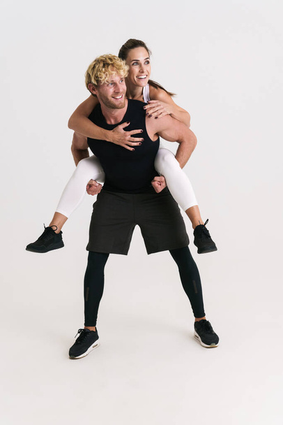 European man and woman in sportswear piggybacking and laughing isolated over white background - Fotó, kép
