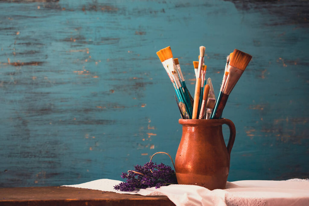 Still life of paint brushes  in clay jug an lavender flower on vintage turquoise background - Valokuva, kuva