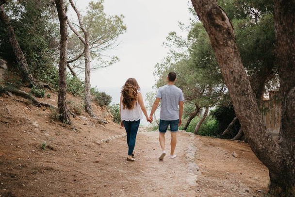 A photo from behind of a Hispanic man and his Latina girlfriend who are descending from the wooded in a highland park in Spain. A couple of tourists are enjoying each other in Valencia - Fotografie, Obrázek
