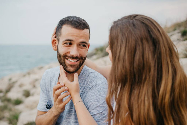Latina tyttö silitti käsillään hymyilevän poikaystävänsä kasvoja Espanjan kallioisella rannikolla. Pari turistia pelleilee illalla ylämaan puistossa Valenciassa. - Valokuva, kuva