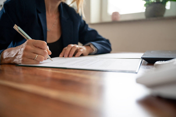Tiefansicht einer Geschäftsfrau, die an ihrem Schreibtisch im Büro sitzt und einen Vertrag oder ein Rechtsdokument unterschreibt. - Foto, Bild
