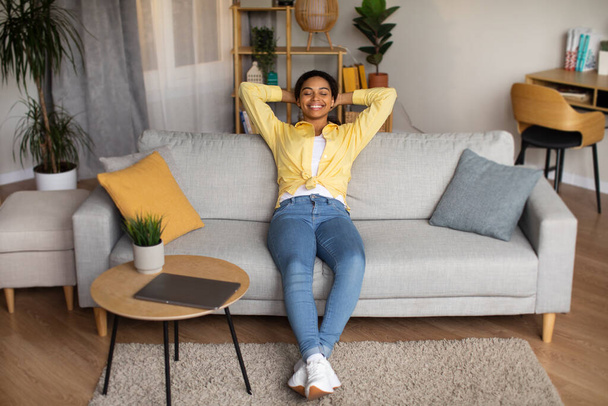 Relaxed African American Female Resting Sitting On Sofa Near Table With Laptop Relaxing After Work, And Enjoying Domestic Comfort Posing With Eyes Closed In Living Room At Home. Full Length - Photo, Image