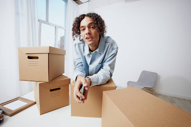 guy with curly hair cardboard boxes in the room unpacking with phone Lifestyle. High quality photo - Photo, Image