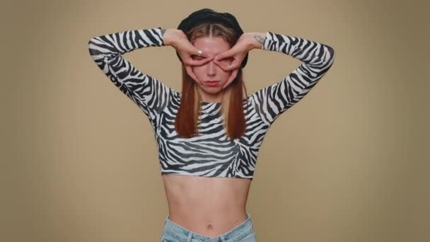 Lovely pretty funny woman in crop top making playful silly facial expressions and grimacing, fooling around, showing tongue. Adult stylish female girl isolated alone on beige studio background indoors - Metraje, vídeo