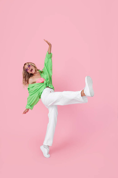 Full length view of pretty cheerful girl dancing in good mood in green bright shirt isolated on pink background - Fotografie, Obrázek
