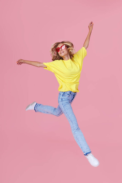Full length portrait of a joyful young woman in casual clothes jumping and celebrating on a pink background - Foto, Imagem
