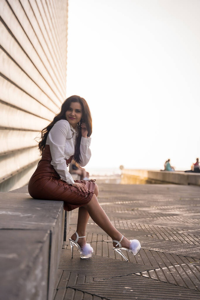Brunette woman in a leather skirt sitting in the city on a sunset - Fotoğraf, Görsel