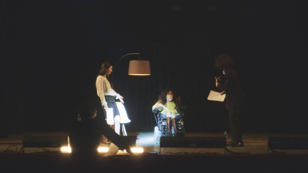 A troupe of actors with disabled woman in a wheelchair, rehearsing a comedy play on a stage in a dark theater with a director together - Φωτογραφία, εικόνα