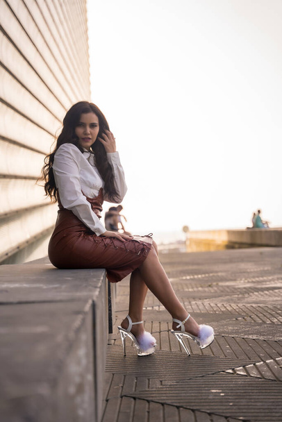 Latin brunette woman with a leather skirt sitting in the city on a sunset - Foto, Imagen
