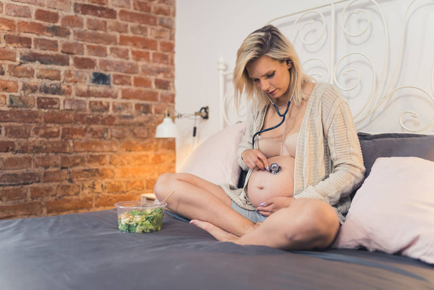 pregnant Caucasian woman trying to listen to her babys heartbeat in the bedroom, pregnancy concept. High quality photo - Foto, Bild