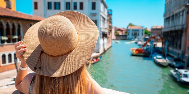 Kobieta w kapeluszu stojąca na moście w Wenecji w słoneczny letni i świąteczny dzień. - Zdjęcie, obraz