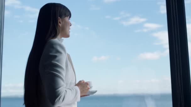 Розслаблена жінка відпочиває каву з видом на океан крупним планом. Бізнес-леді, що тримає чашку еспресо, п'є біля панорамного вікна розкішного готелю. Сниться людина-лідер з видом на морський горизонт після робочого дня
  - Кадри, відео