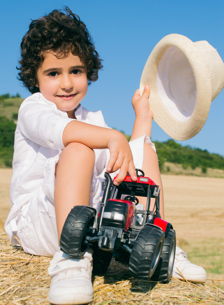 Little boy in a hat sitting on hay roll with toy - Photo, Image