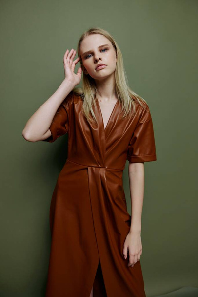Seksikäs ammatillinen blondi malli nahka ruskea paletti vaatteita koskettaa hiukset kädestä päähän tarkastellaan kameran poseeraa yli vihreä studio tausta. Tyylikäs muotokuva bannerin suunnitteluun - Valokuva, kuva