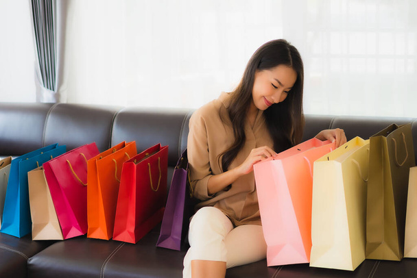 Portré gyönyörű fiatal ázsiai nő online vásárlás hitelkártyával és okostelefon körül bevásárló táska a nappaliban - Fotó, kép