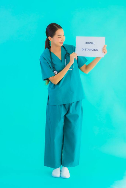 Retrato bonito jovem asiático médico mulher mostrar sinal com Social distanciamento no azul isolado fundo
 - Foto, Imagem