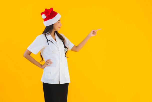 Πορτρέτο όμορφη νεαρή ασιάτισσα γιατρός γυναίκα φορούν Χριστούγεννα ή Σάντα καπέλο σε κίτρινο απομονωμένο φόντο - Φωτογραφία, εικόνα