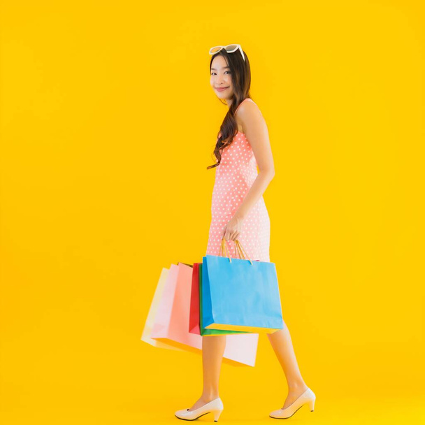 デパートのカラフルなショッピングバッグと黄色の隔離された背景にショッピングモールと肖像画の美しい若いアジアの女性 - 写真・画像