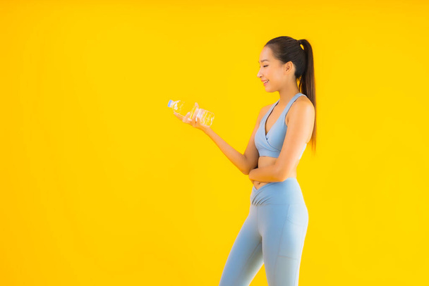 Портрет красивая молодая азиатская женщина с бутылочной водой на желтом изолированном фоне
 - Фото, изображение