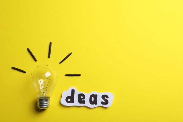 Word Ideas made with lightbulb and paper sheet on yellow background, flat lay. Space for text - Photo, image