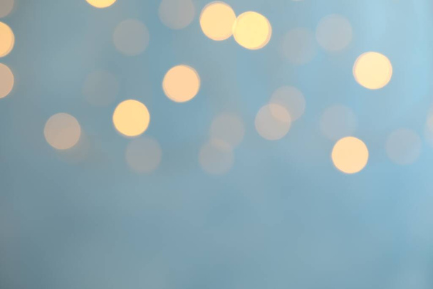 Blurred view of festive lights on light blue background. Bokeh effect - Photo, Image