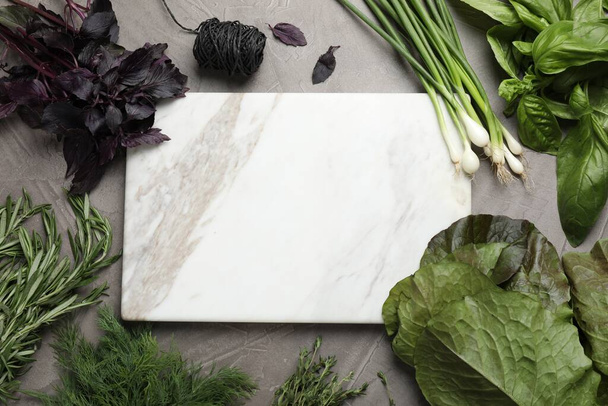 Different herbs and marble cutting board on grey table, flat lay. Space for text - Fotoğraf, Görsel
