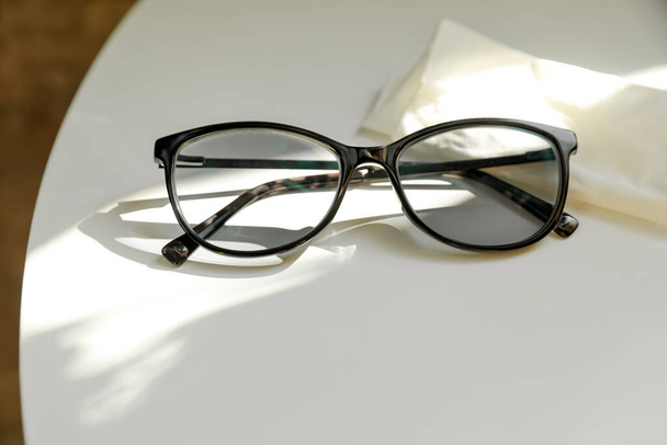Stylish black eye glasses and cloth on white table. Space for text - Photo, image