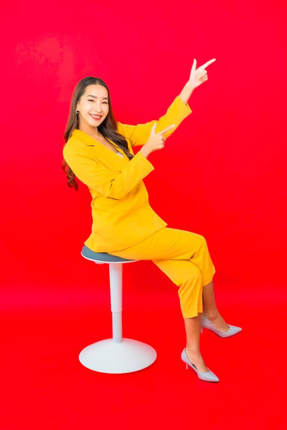 Portrait belle jeune femme asiatique d'affaires s'asseoir sur la chaise avec le sourire sur fond rouge - Photo, image