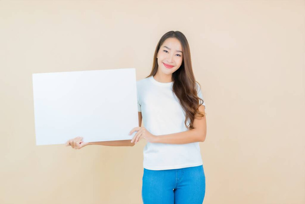 Portrait belle jeune asiatique femme montrer vide blanc panneau d'affichage carte papier sur fond crème - Photo, image