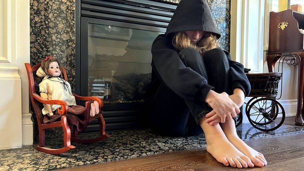 offended teenager teenager girl sitting by the fireplace with her legs bent and her head bowed she pulled the hood over her face she has a black sweatshirt and black jeans sadness of adolescence - Photo, Image