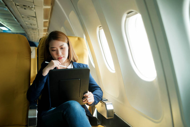 Молодая деловая женщина в самолете, использующем ноутбук во время полета самолета, концепция путешествия. - Фото, изображение