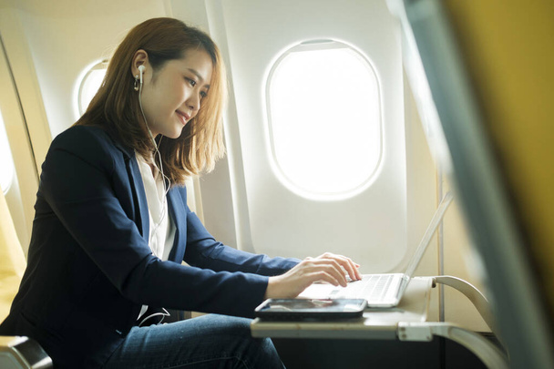 Uçakta dizüstü bilgisayar kullanan genç bir iş kadını. Bir uçak uçuşunda seyahat konsepti.. - Fotoğraf, Görsel
