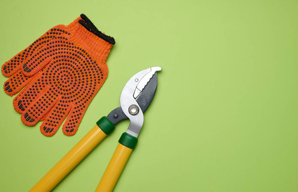 Large garden pruner for pruning branches on trees and orange textile gloves on a green paper background, copy space - Foto, Imagem