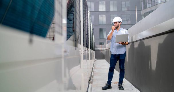 Професійний інженер або технік людина використовує ноутбук і walkie-talkie, щоб зв'язатися зі своїм співробітником про рішення свого проекту і залишитися на терасі високої будівлі
. - Фото, зображення
