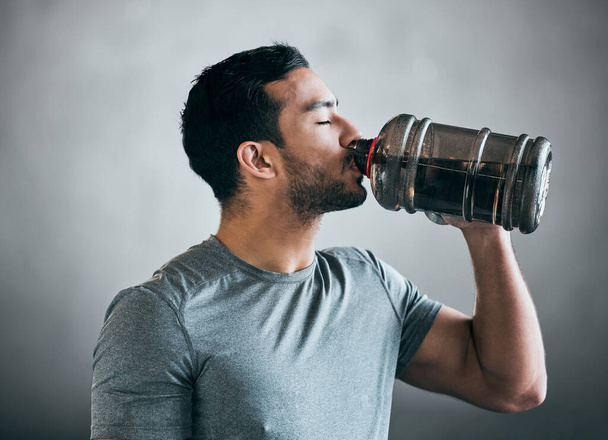Bleiben Sie während seines Aufwärmens hydratisiert. ein hübscher junger männlicher Athlet, der vor grauem Hintergrund Wasser trinkt - Foto, Bild