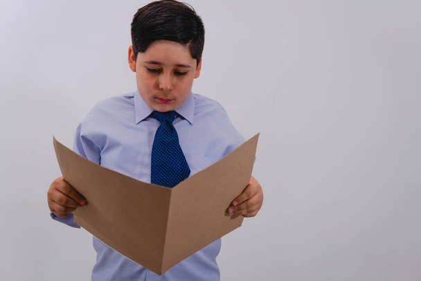Een jongen gekleed in een pak en stropdas die doet alsof hij een zakenman is terwijl hij een map leest met belangrijke papieren. Een jongetje verkleed als zakenman.. - Foto, afbeelding