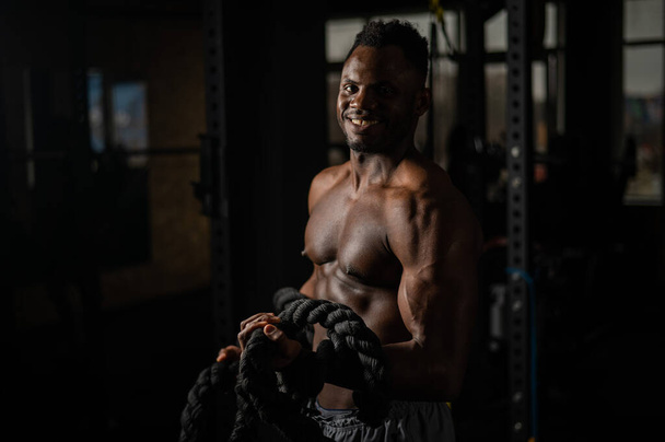 Muscular african american man posing with rope in gym - Photo, image