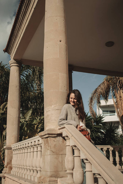 A young woman stands and enjoys near the old building with columns and tropical plants in Larnaca, Cyprus. - Fotó, kép