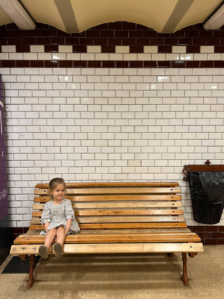 Little girl sitting on a wooden bench in the subway. High quality photo - Φωτογραφία, εικόνα