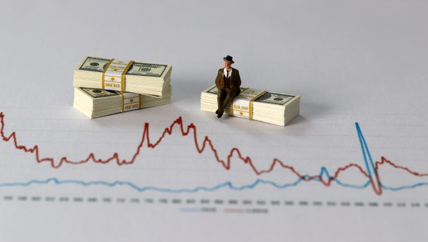 Business concept with graphs and miniature. A bundle of money with a miniature man on a graph. - Fotografie, Obrázek