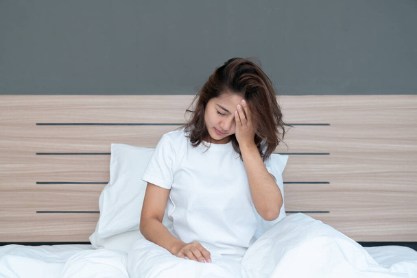 Nuori aasialainen naiset makaa sängyssä pitäen päätään ottaa voimakas päänsärky ehkä migreeni aamulla sängyllä - Valokuva, kuva