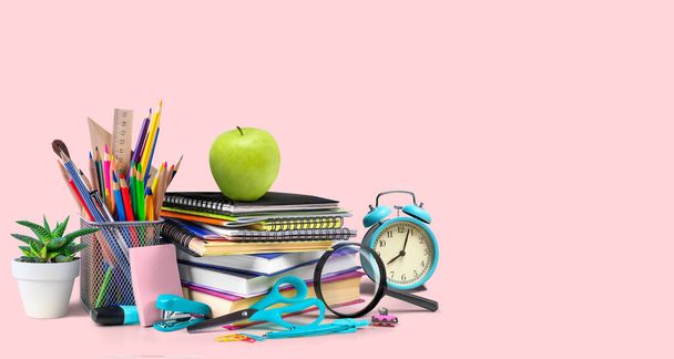 School supplies composition with alarm clock and apple on a pink background - Photo, image