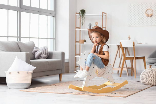 Cute little girl in hat and vest playing with rocking horse at home - Φωτογραφία, εικόνα